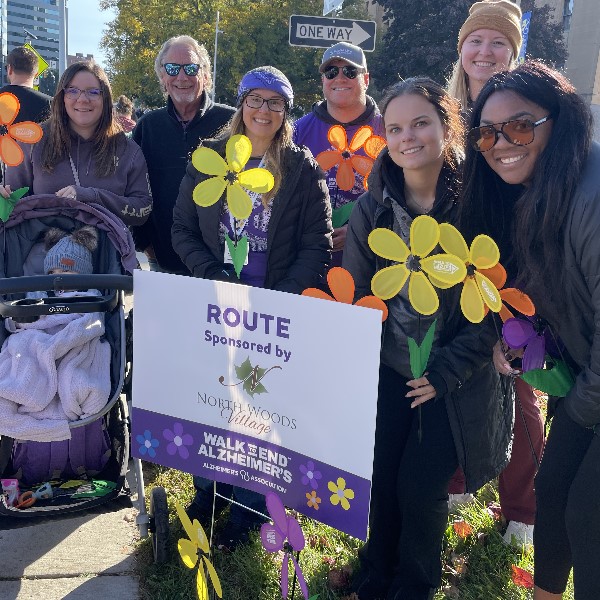 Participants in the Walk to End Alzheimers event, smiling and holding large yellow and orange stylized flower props